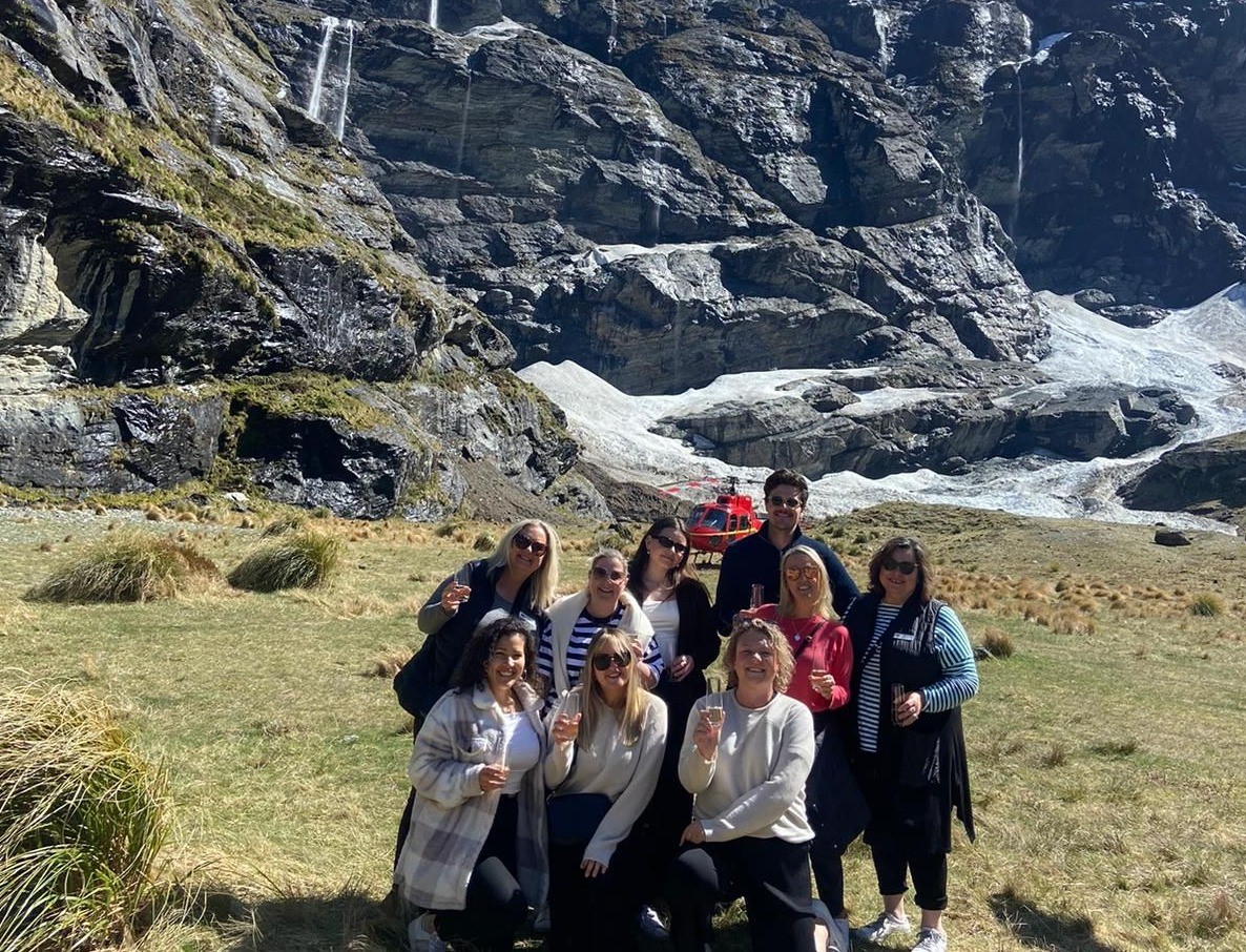 Group with a glass of bubbles at Earnslaw Burn. Waterfalls and glacier in the background.