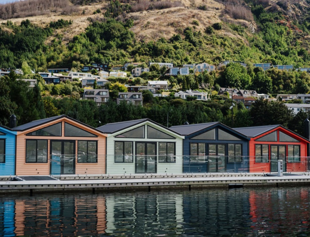 Queenstown Marina sheds on the lake, with apartments and greenery in the background. 