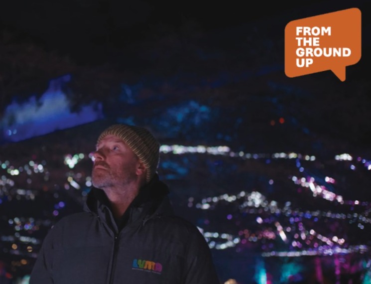 Man looking upwards with Queenstown at night in the background.