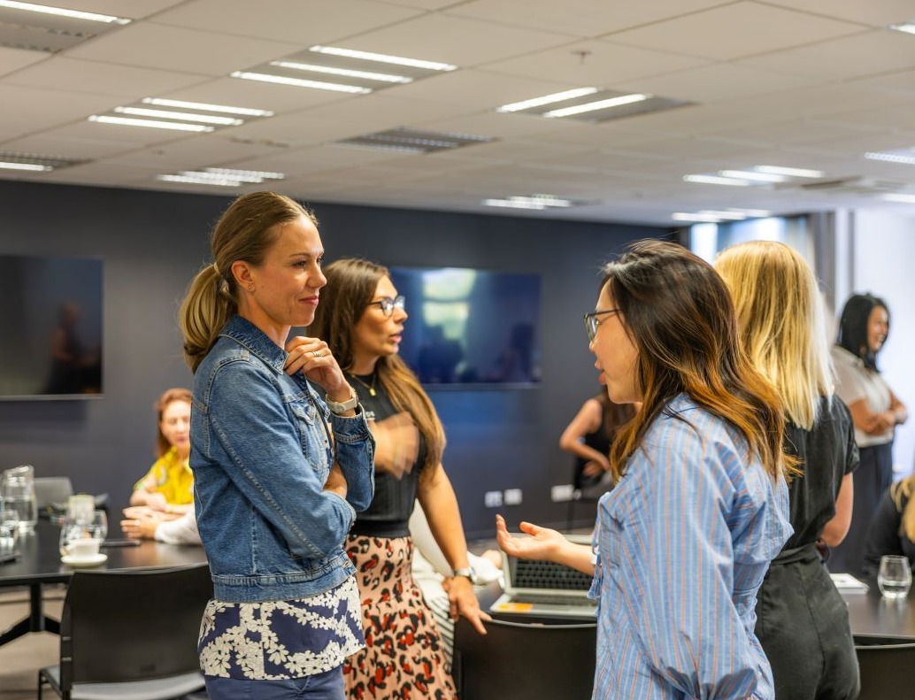 Tourism New Zealand Business Events' Global Manager, Penelope Ryan and a Queenstown supplier talking. Other people networking in the background at Destination Queenstown office.