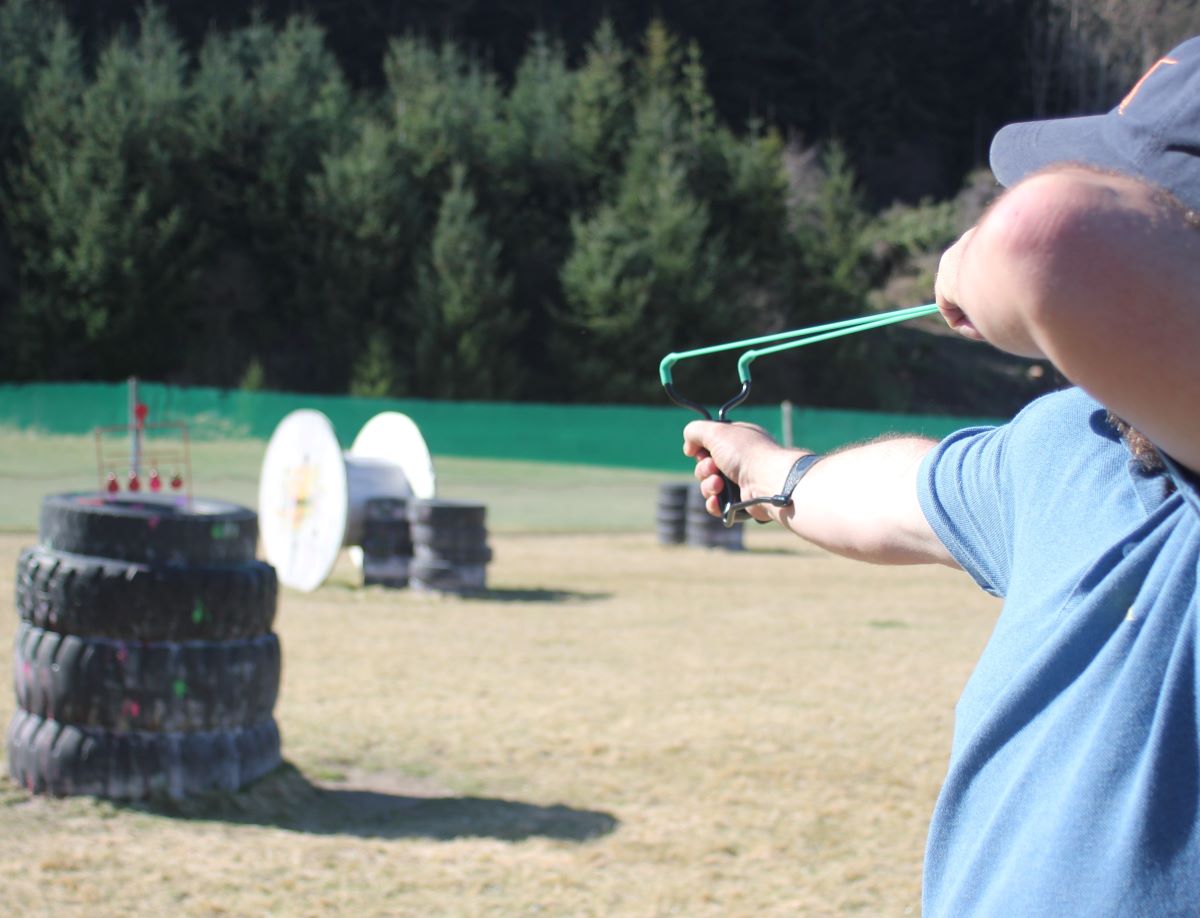 man aiming with a sling shot at a pile of tyres at The Playground.